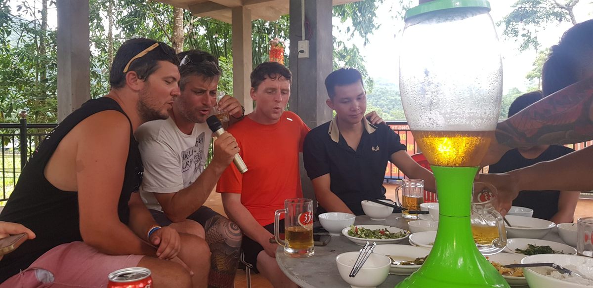 Riders and hosts around a table, one of them singing into a microphone
