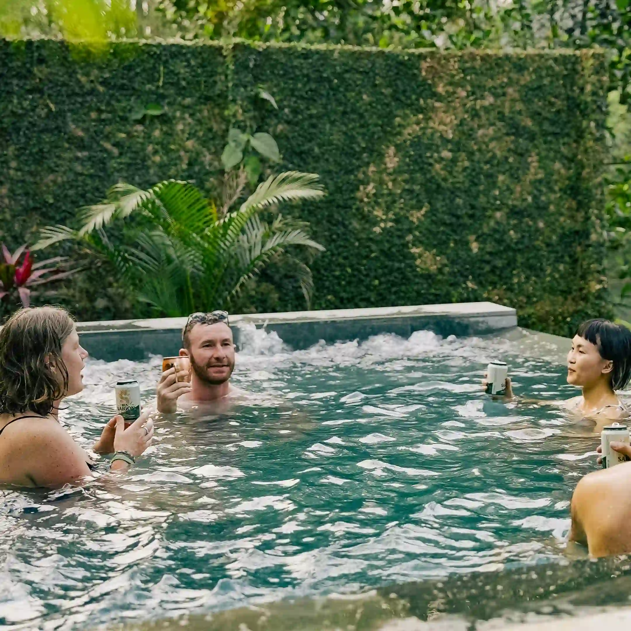 Three people sitting in the hot tub with drinks, the jets running