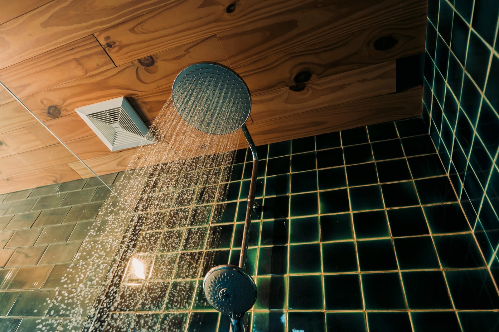 Rainfall shower running over dark green tiles under a timber ceiling