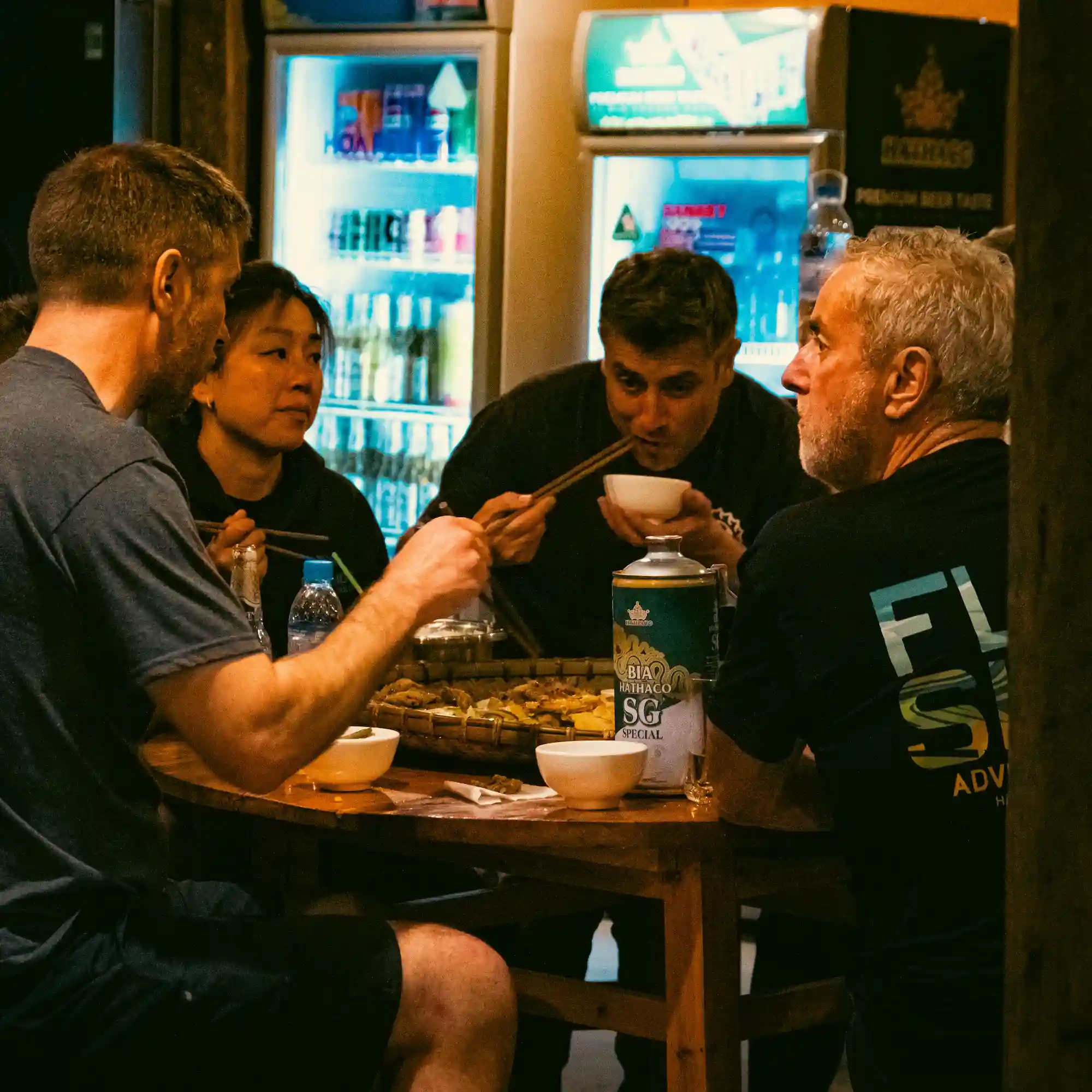 Linh and Tom eating with guests around a table at a roadside spot