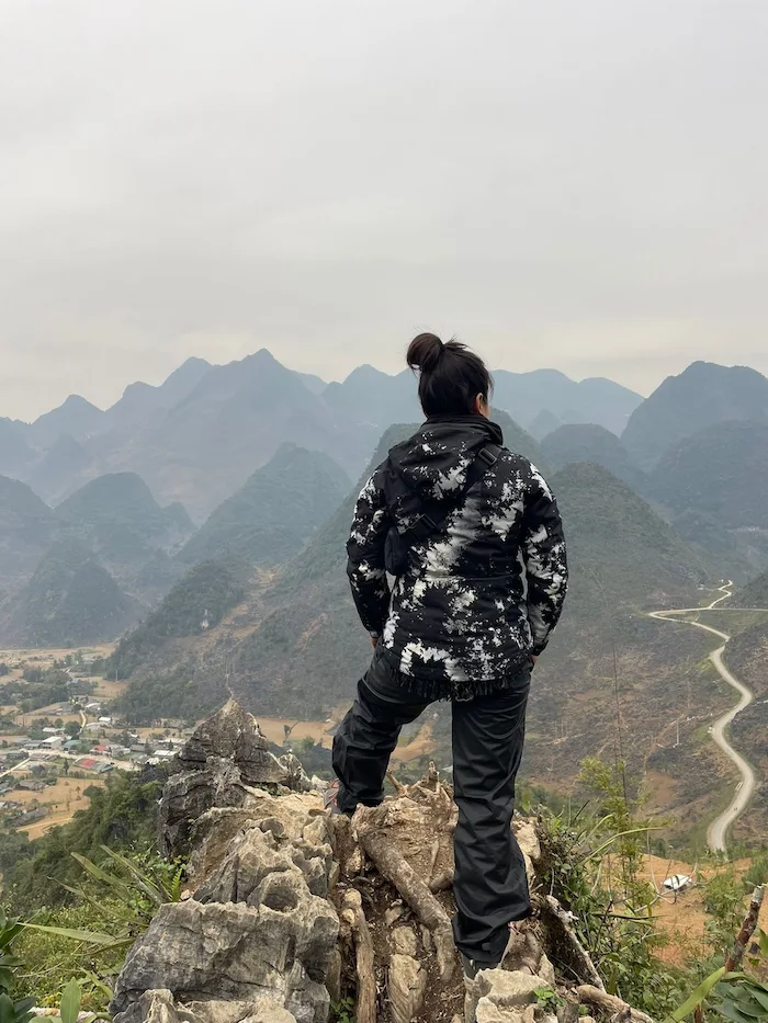 A rider standing on a rocky outcrop, back to the camera, looking out over the mountains