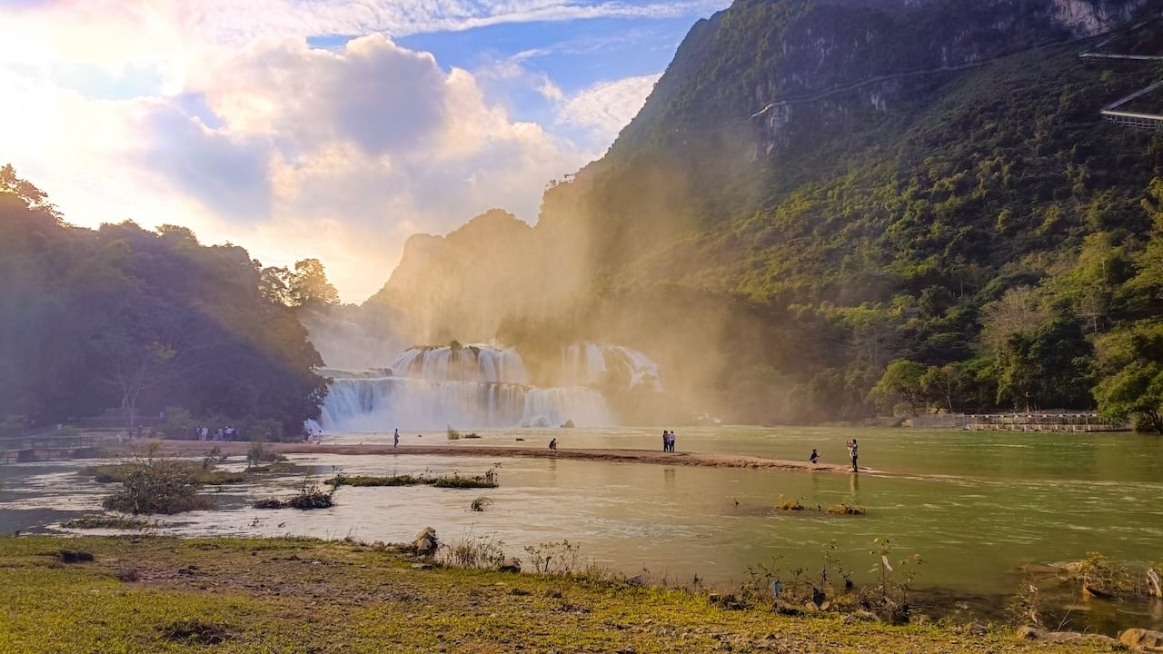 A wide waterfall in the early light, with people on the sandbank