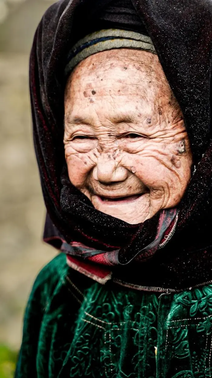 An elderly Hmong woman in a headscarf, smiling at the camera