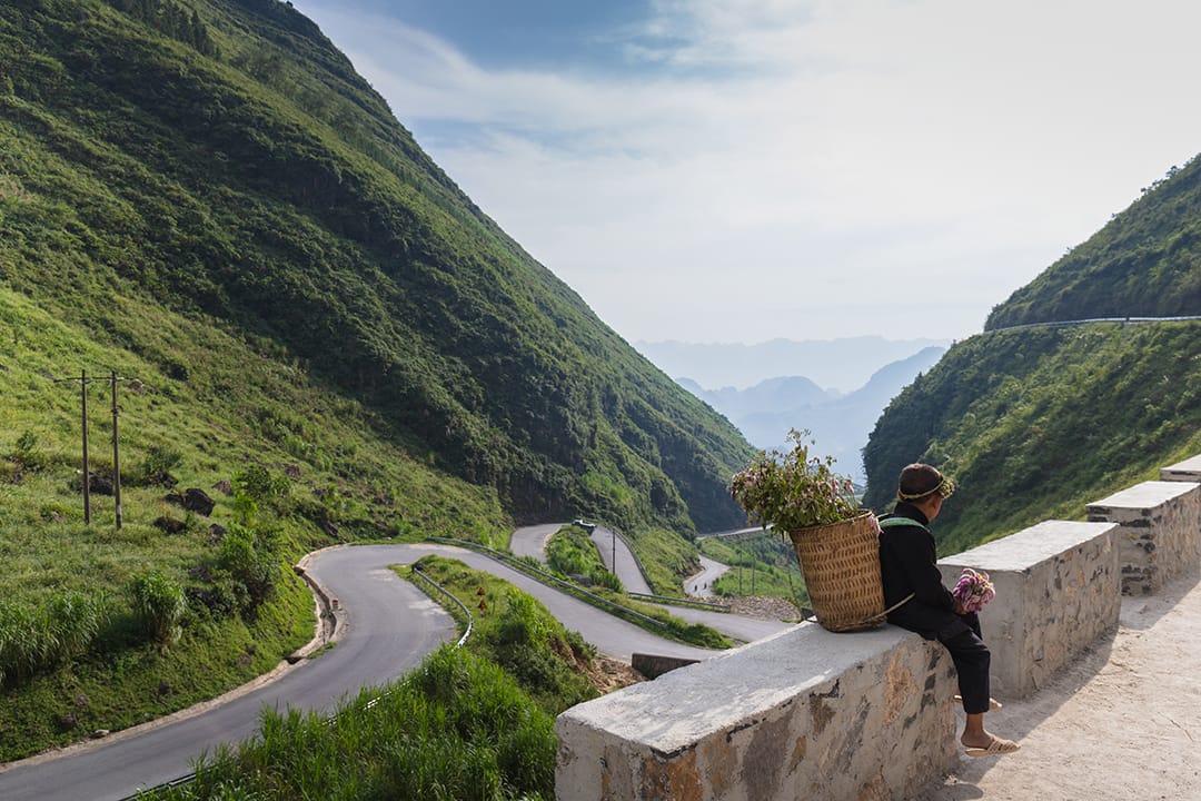 A boy sitting on a wall above the road switchbacking through the pass